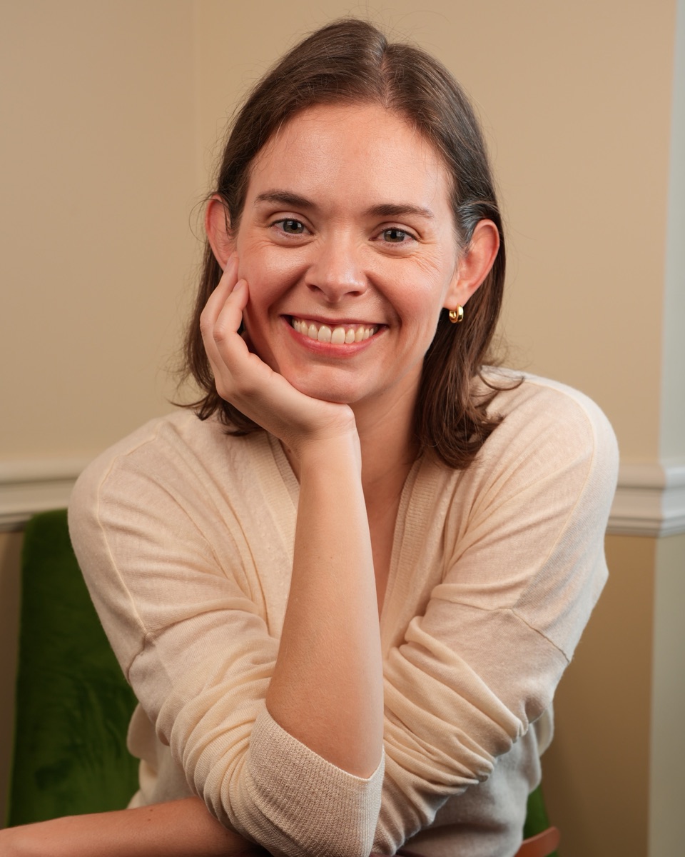 Lee Mullins, laughing, chin on hand, in a green velvet chair